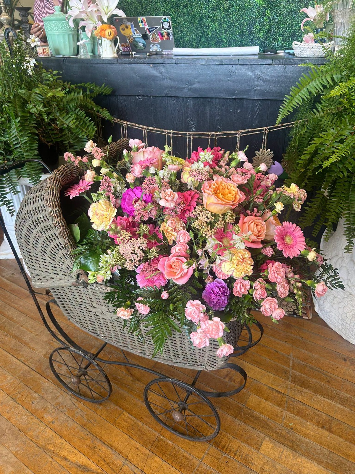 A vintage wicker pram overflowing with pink roses, gerbera daisies and carnations